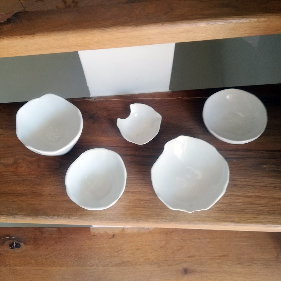 Five white ceramic bowls on wooden stairs.