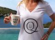 Woman wearing white t-shirt with black logo and holding white ceramic cup with black letters in front of a pool and the sea.