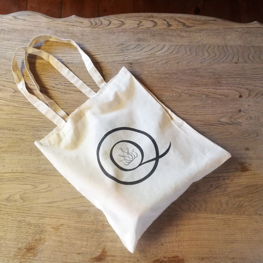 White cotton tote bag with black logo on wooden surface