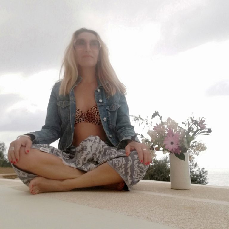 Cross-legged woman sitting next to vase with flowers