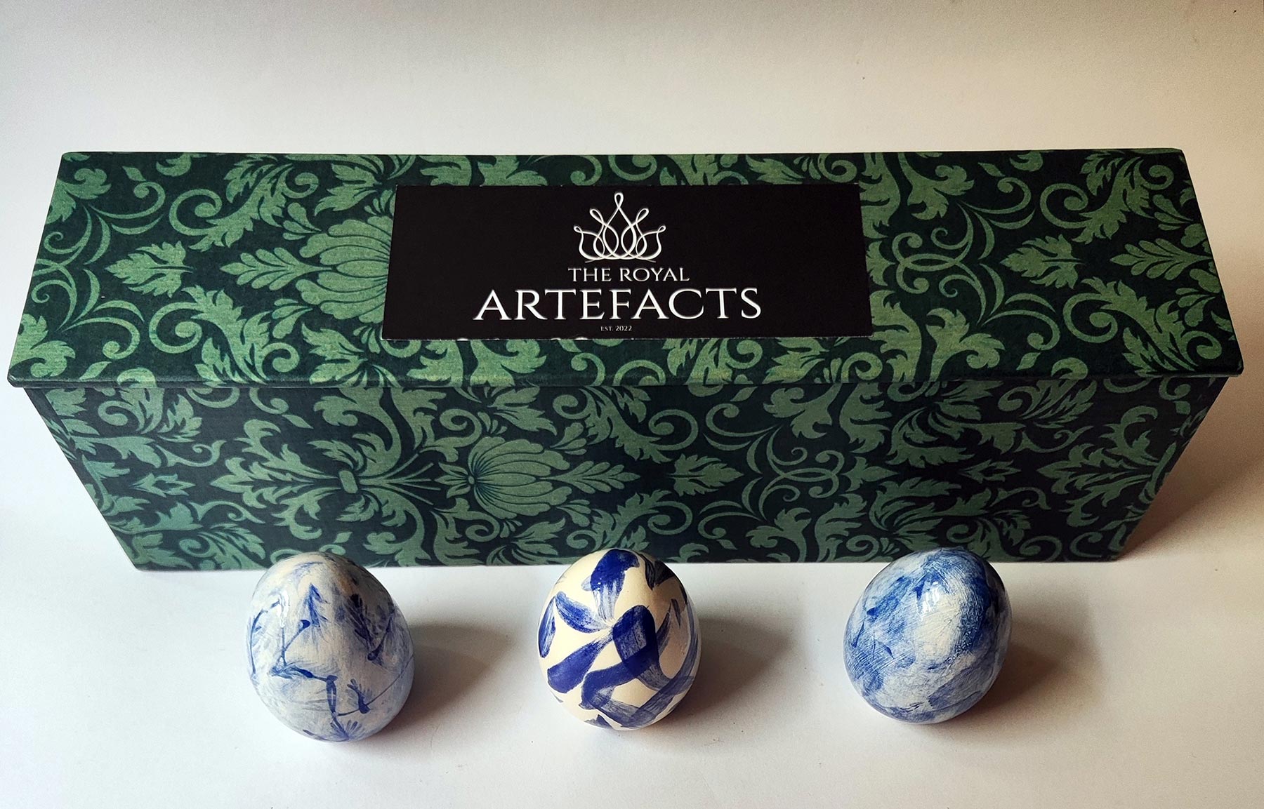 The Royal Artefacts Easter Eggs Three blue ad white ceramic eggs and a patterned green box with The Royal Artefacts logo
